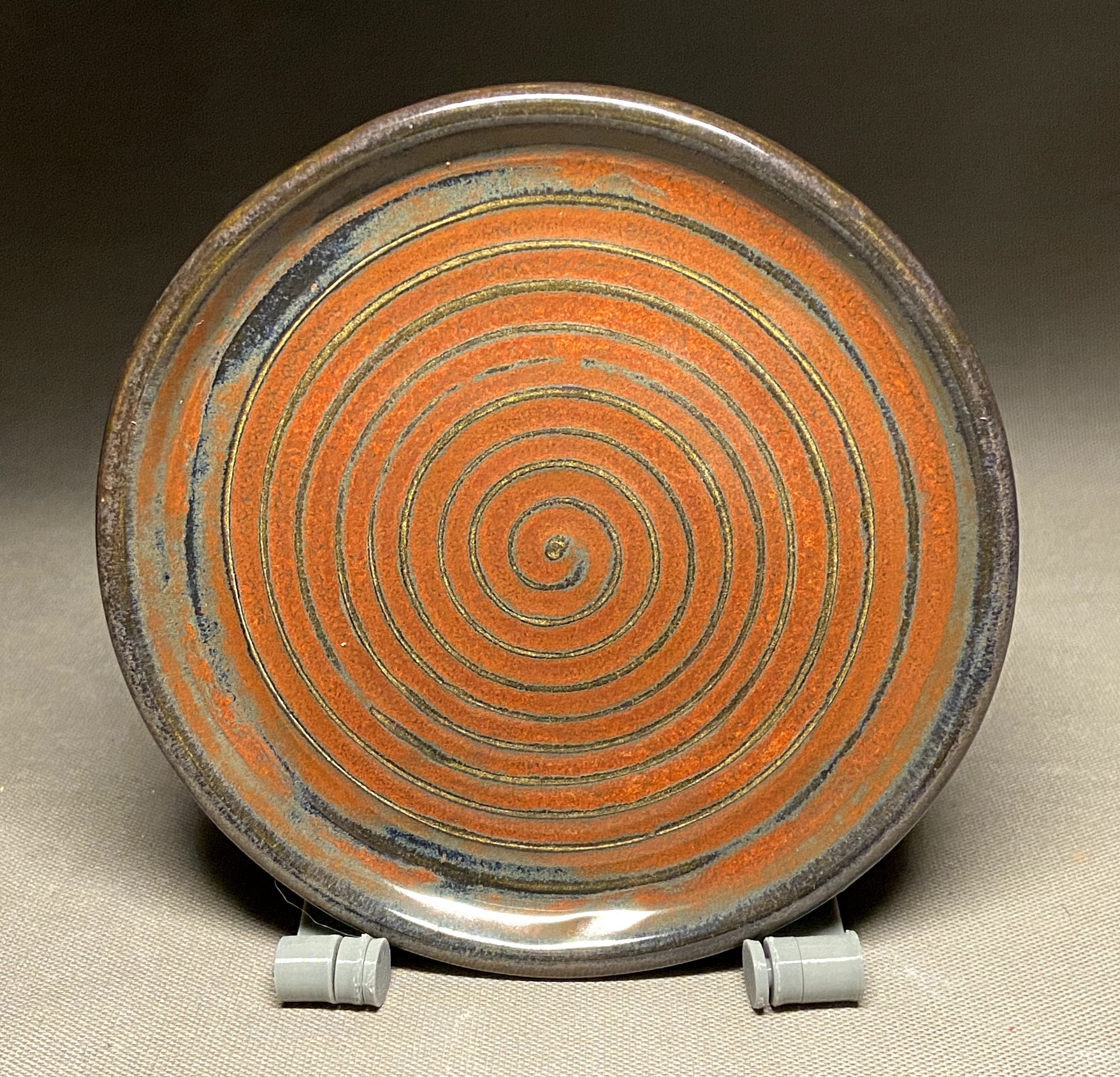 Handmade ceramic spiral plate with orange and blue surface detail